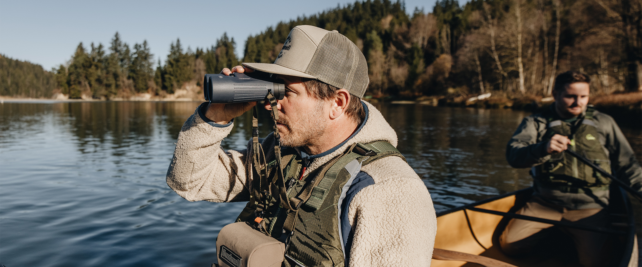 Two men in a canoe on a lake, one using binoculars.