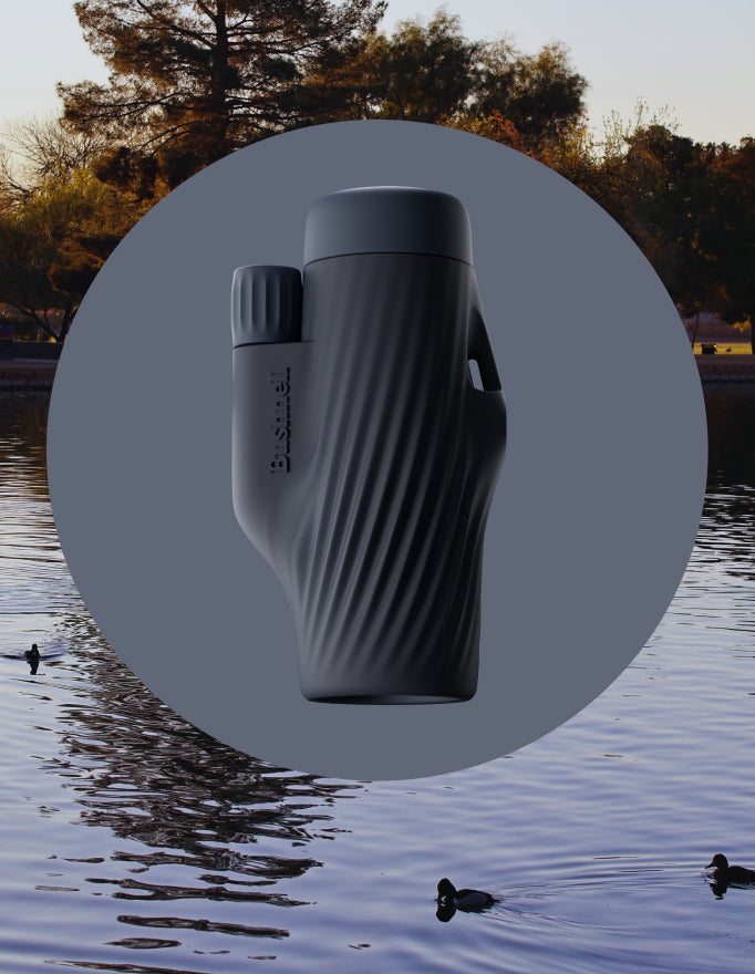 Black binoculars on a circular overlay with a natural background of water and trees.