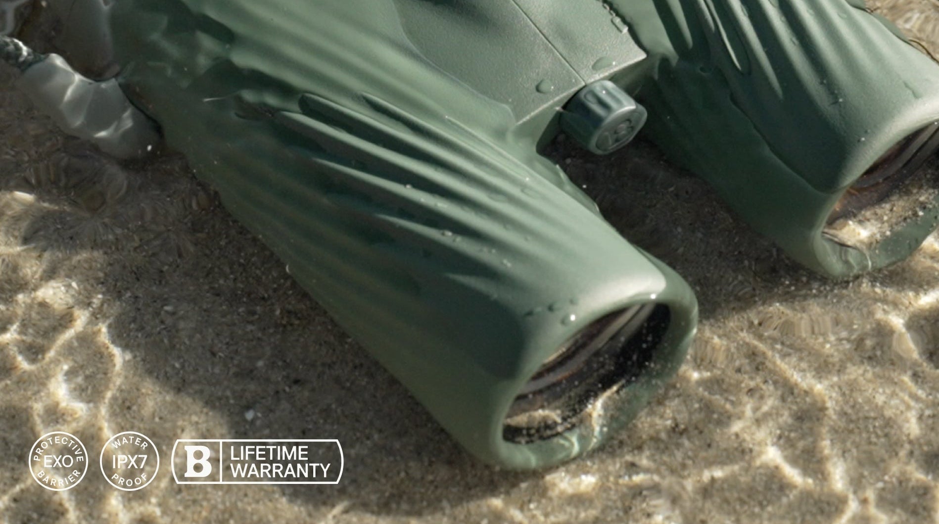 Green binoculars on a sandy surface with a brand logo and text.