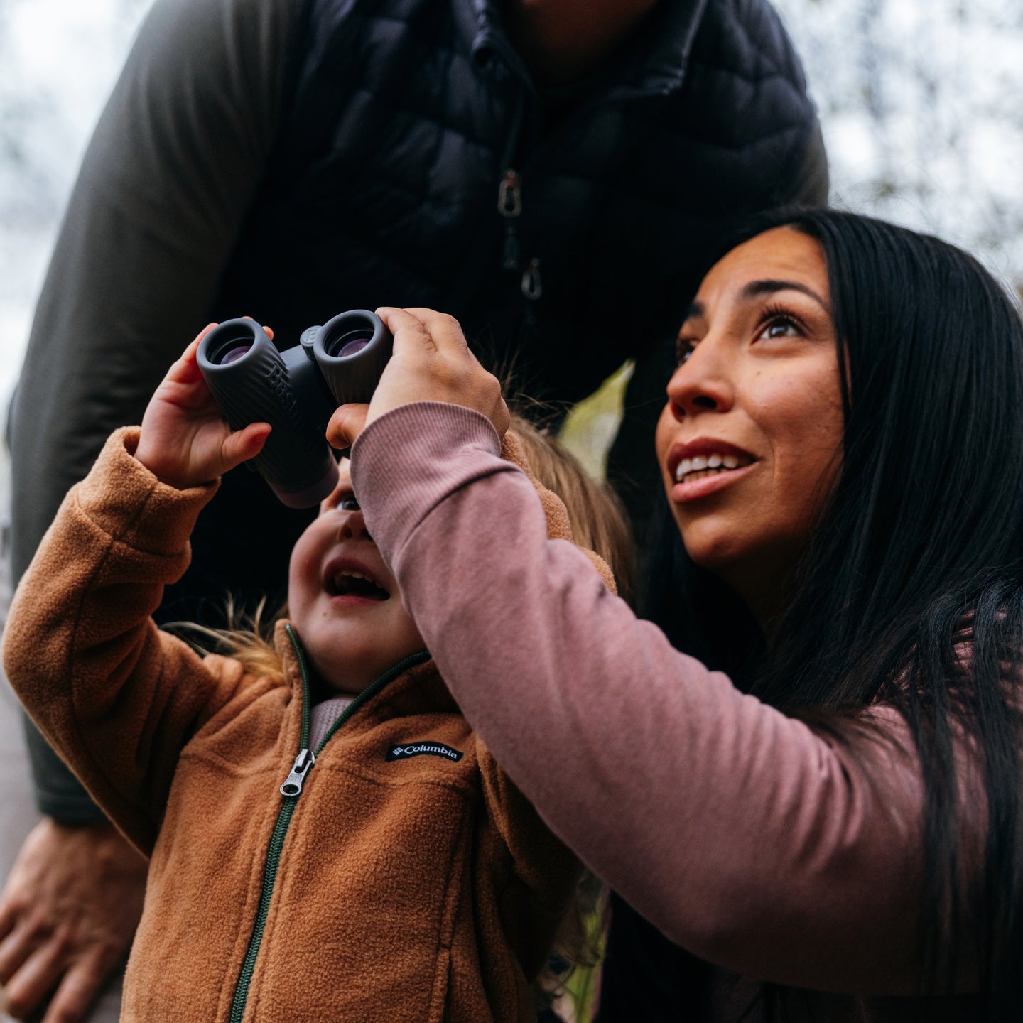 Woman assisting a child with Bushnell binoculars in an outdoor setting