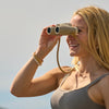 Blonde woman in a tank top using Bushnell A1 binoculars with a clear sky background