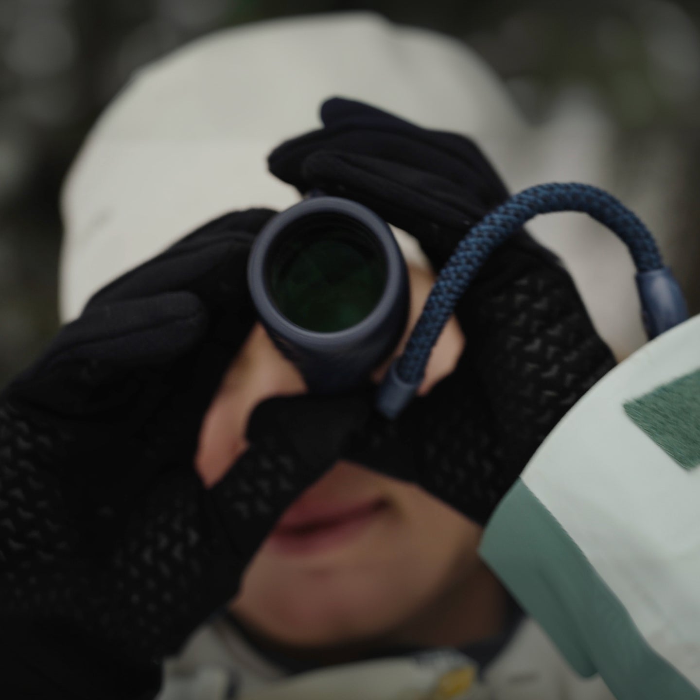 Person wearing gloves holding a Bushnell A3 monocular with a blurred natural background
