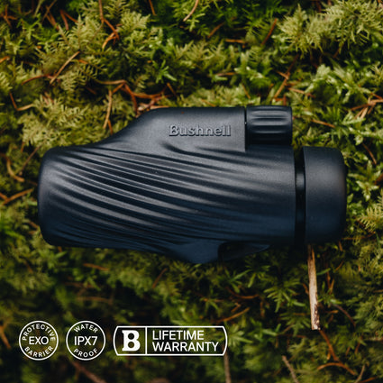 Black Bushnell monocular on a green mossy background with product features displayed.