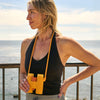 Woman with orange A3 binoculars and matching neck strap hanging around her neck with a scenic ocean view in the background