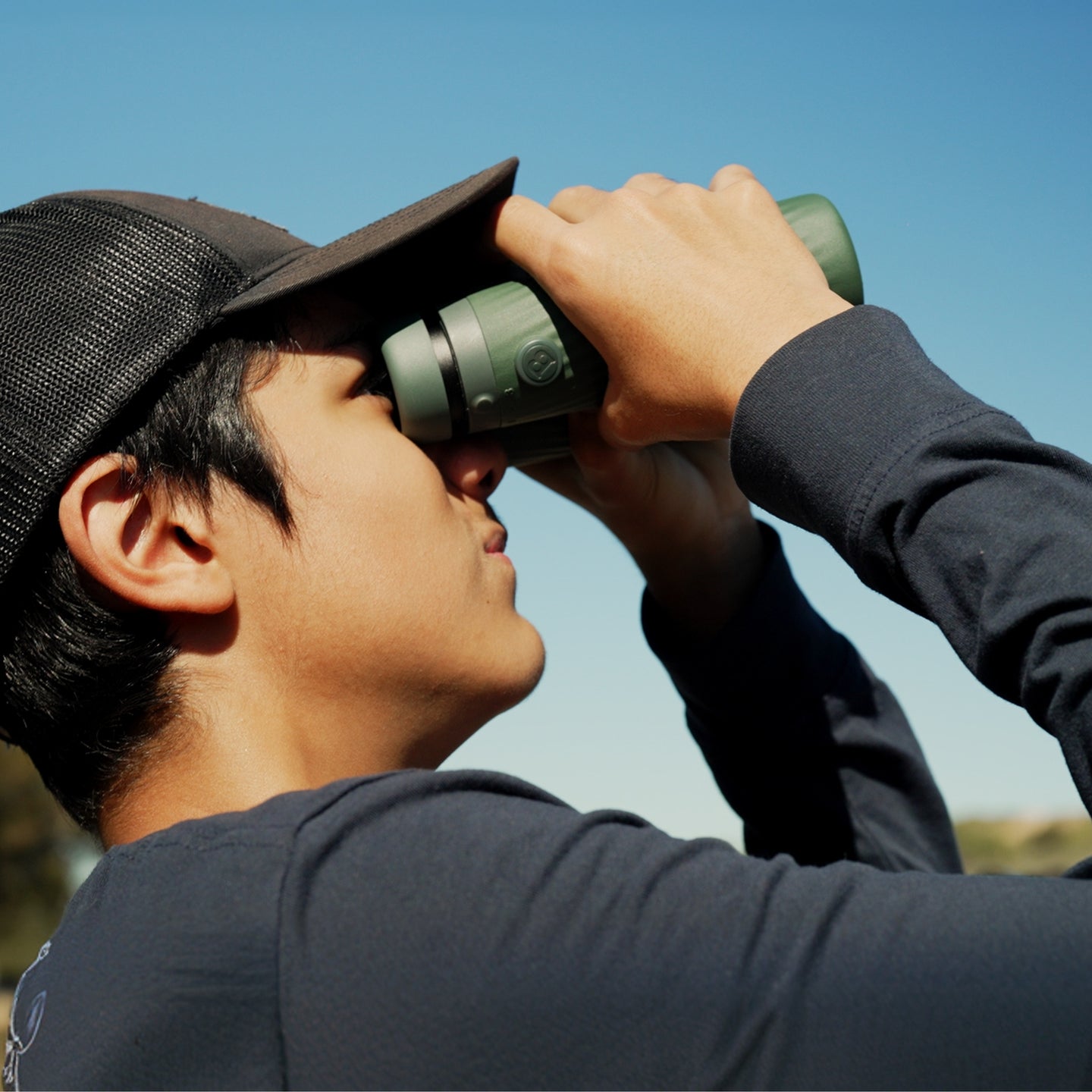 Person using Bushnell A5 binoculars in color against a clear blue sky