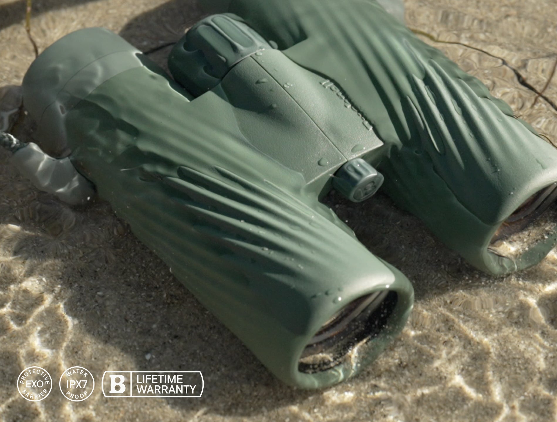 Green binoculars on a sandy surface with a brand logo and text.