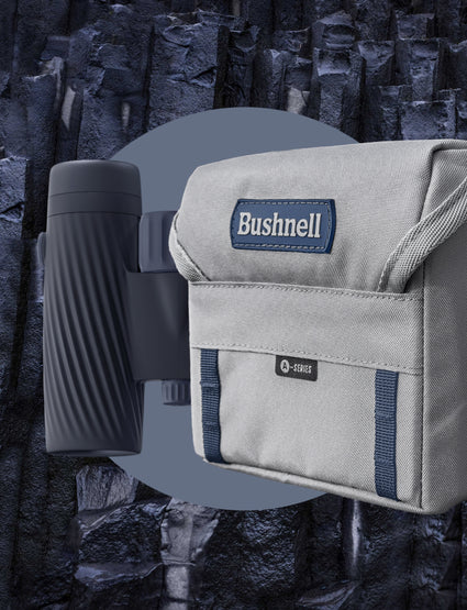 Binoculars with a carrying case featuring Bushnell branding against a rocky background