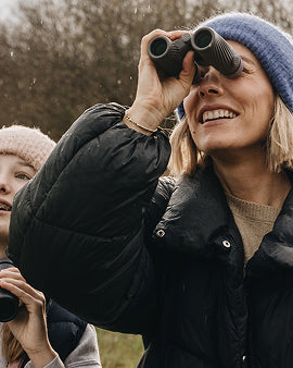 Woman using binoculars with a child in a natural setting