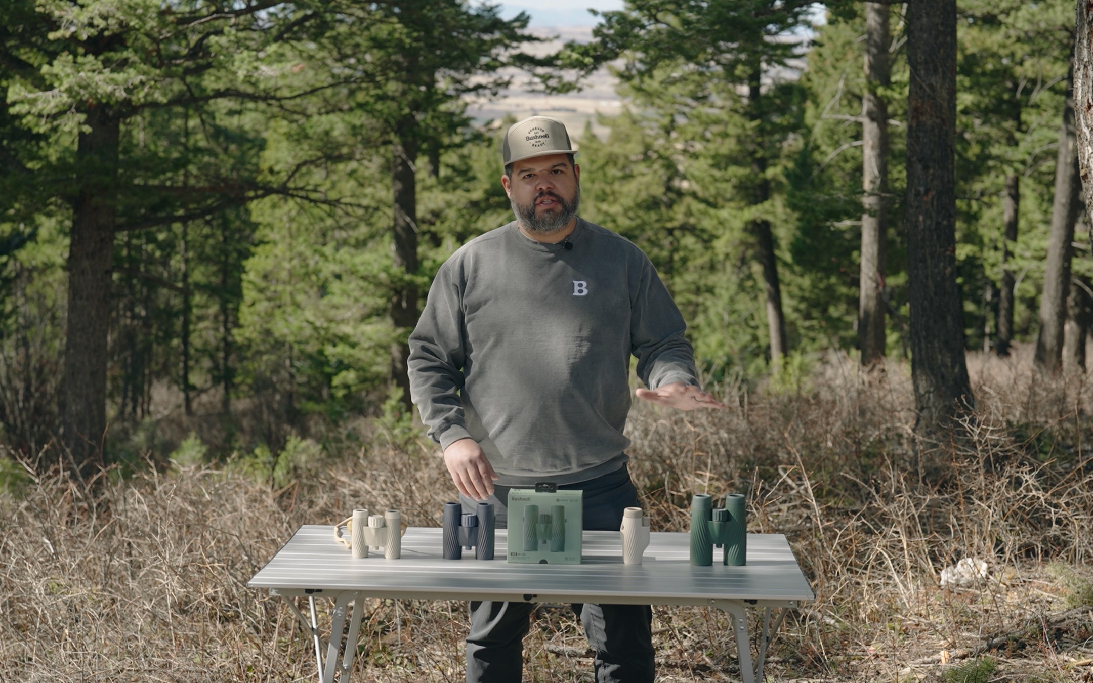 Man standing outdoors with a table displaying binoculrs in a forest setting